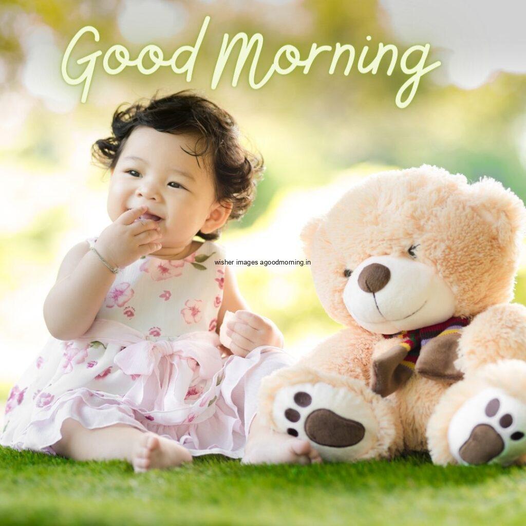 Baby girl Sitting with light brown color teddy good morning quote is placed