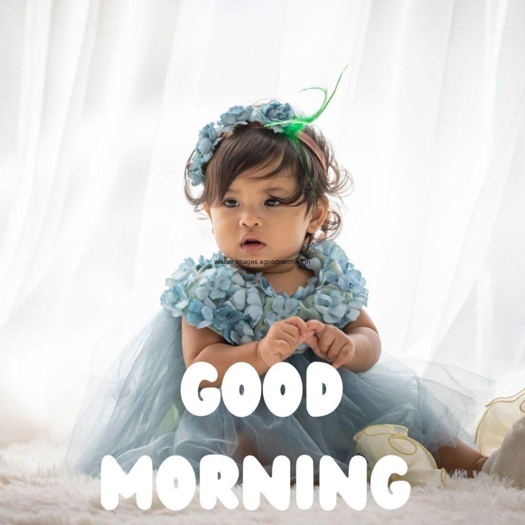 Baby girl wearing the blue clothes behind the white background good morning quote is placed