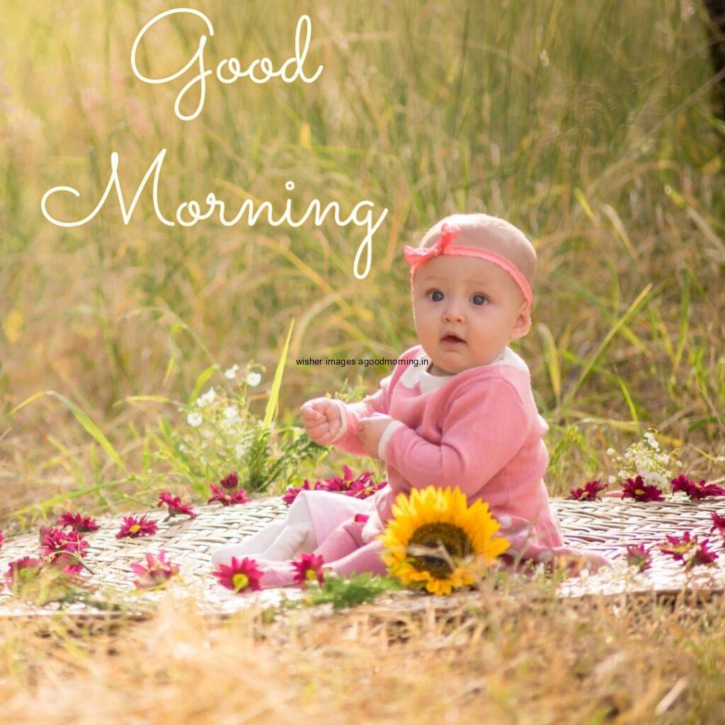 Baby girl wearing the white dress and sitting on the pink flowers mat good morning quote is placed