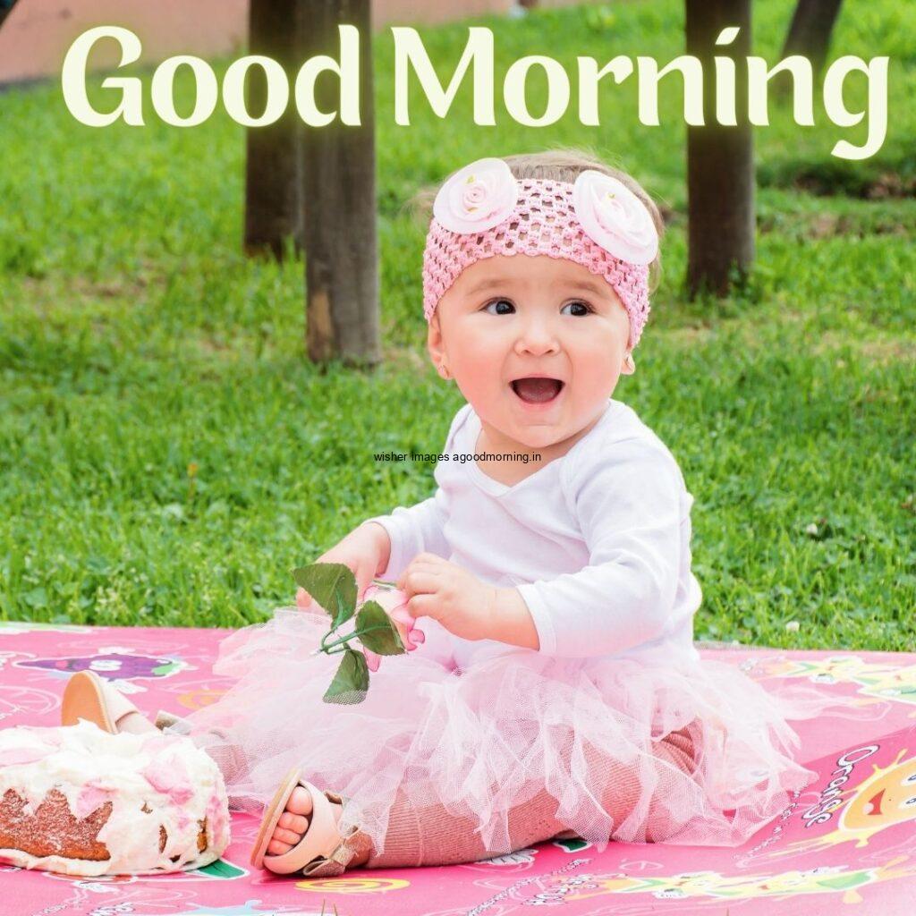 Baby girl wearing the white dress and sitting on the pink mat good morning quote is placed