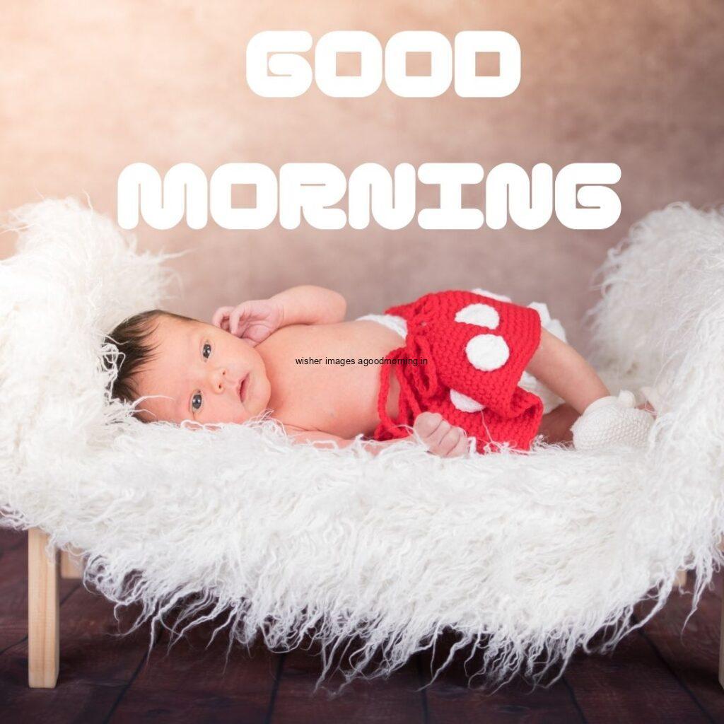 Baby girl with red pant on the bed good morning quote is placed