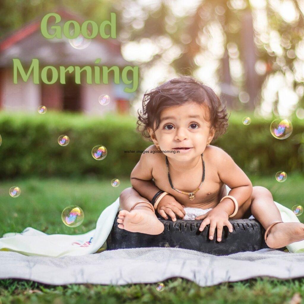 smiling baby seen in front, background is setup with grass good morning quote is placed