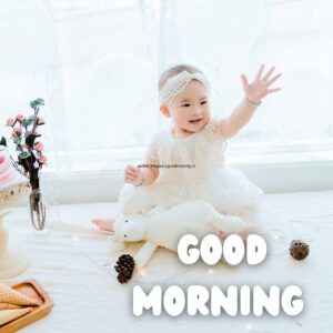 White dress wearing the baby girl, beside the girl flowers is setup good morning quote is placed